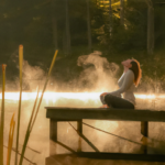 E woman sits cross-legged on weathered wooden dock at golden hour, eyes gently closed in meditation